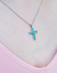 Necklace with a cross emerald pendant featuring green round cut stones on a pink top.