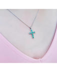 Emerald cross pendant necklace with round-cut emeralds in 18K white gold, worn on a pink top.