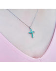 Emerald cross pendant necklace with round-cut emeralds in 18K white gold, worn on a pink top.