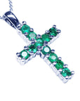 A 18k white gold cross pendant with round cut Colombian emeralds on a topside view position.
