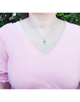 Woman wearing a small round-cut emerald cross pendant necklace on an 18K white gold chain.
