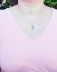 A woman wearing a pink top with a necklace featuring a natural emerald pendant against a blurred green background.