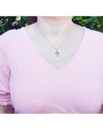 Woman wearing a small round-cut emerald cross pendant necklace on an 18K white gold chain.