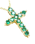 A cross pendant on a right-side position and top view of eleven round cut emeralds prong set in yellow gold