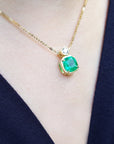 Gold necklace with a natural emerald pendant on a person wearing a navy-blue top.