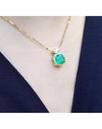 Gold necklace with a natural emerald pendant on a person wearing a navy-blue top.