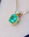 A yellow gold necklace with a cushion emerald pendant on a skin background