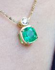Gold necklace with a cushion cut emerald pendant on a person's neck