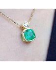 Gold necklace with a cushion cut emerald pendant on a person's neck