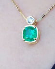 Gold necklace with a cushion cut emerald pendant on a person's neck
