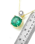 A yellow gold cushion cut emerald and diamond pendant next to a ruler for scale on a white background