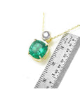 A yellow gold cushion cut emerald and diamond pendant next to a ruler for scale on a white background