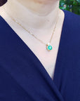 Person wearing a gold necklace with an emerald pendant against a blurred green background