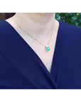 Woman wearing a vibrant deep bluish-green emerald cushion cut pendant in 18K yellow gold.
