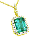 the topside view of a natural colombian emerald pendant emerald-cut surrounded by a halo diamond in 18k yellow gold.