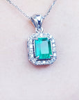A white gold emerald pendant with a halo diamond on a light pink background.