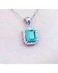 Emerald-cut emerald pendant with halo diamonds in 14K white gold on a delicate chain.