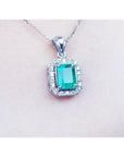 Emerald-cut emerald pendant with halo diamonds in 14K white gold on a delicate chain.