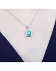 Emerald-cut emerald pendant with halo diamonds in 14K white gold, worn on a model.