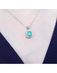 Emerald-cut emerald pendant with halo diamonds in 14K white gold, worn on a model.