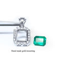14K white gold halo diamond pendant mounting next to a loose emerald-cut Colombian emerald.