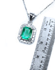 Emerald gemstone pendant on a white gold chain with a ruler for scale on a white background.