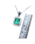 Emerald-cut Colombian emerald pendant with halo diamonds in 14K white gold, shown with a ruler for scale.