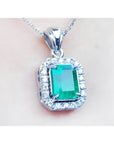 A close-up of an emerald gemstone pendant with white gold and diamonds frame on a light pink background.