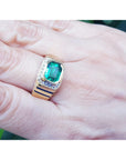 A gold genuine colombian emerald ring being worn by a hand between fingers.