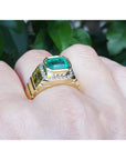 Gold ring 18k for men with a colombian emerald on a hand against a blurred green background.