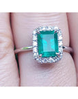 A natural Muzo colombian emerald ring with halo diamond in white gold on a finger.
