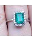 A natural Muzo colombian emerald ring with halo diamond in white gold on a finger.