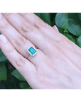 Emerald-cut Muzo emerald ring with halo diamonds in 14K white gold on a hand.