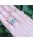 Emerald-cut Muzo emerald ring with halo diamonds in 14K white gold on a hand.