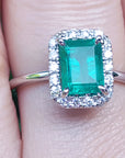 Emerald ring with halo diamond on a finger.