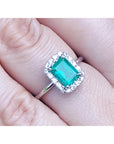 Emerald ring with diamond halo on a finger.