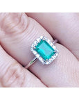 Emerald-cut Muzo emerald halo diamond ring in 14K white gold, worn on a finger.