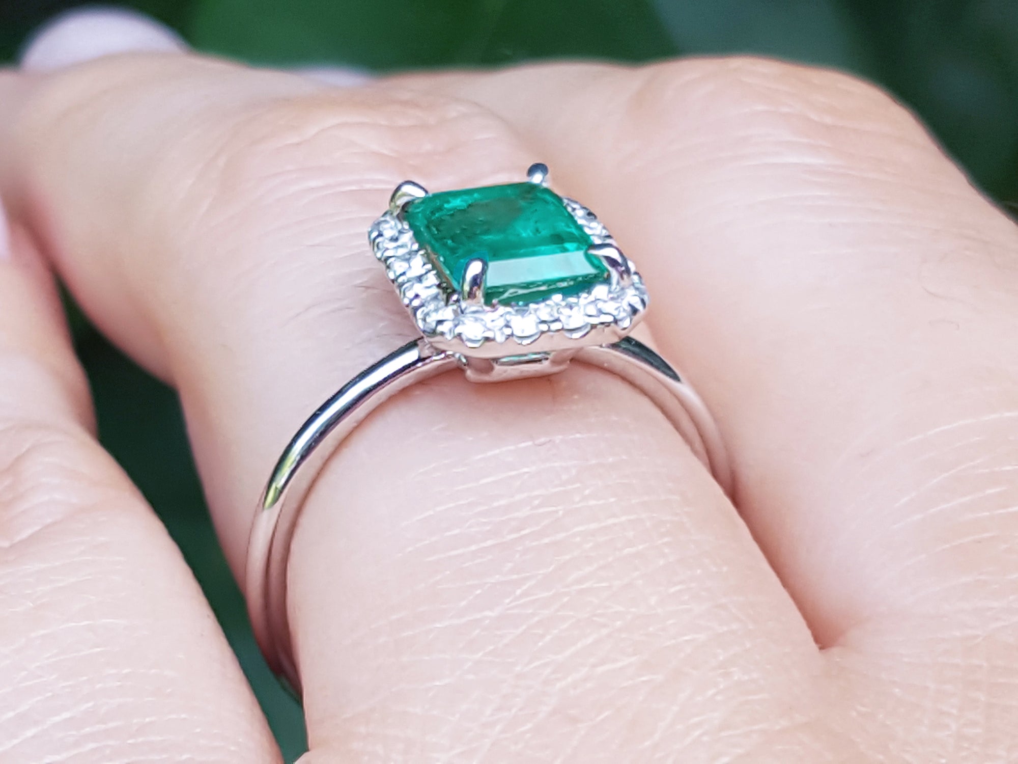 A white gold emerald ring with diamonds accent on a finger.