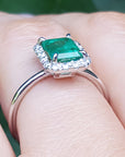 A white gold emerald ring with diamonds accent on a finger.