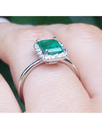 A white gold emerald ring with diamonds accent on a finger.