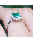 Emerald-cut Muzo emerald halo diamond ring in 14K white gold on a finger.