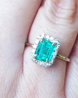A close-up of a halo diamond emerald ring on a person's finger.