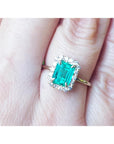 A close-up of a halo diamond emerald ring on a person's finger.