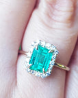 An emerald-cut halo diamond ring in yellow gold in a persons' finger.