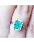An emerald-cut halo diamond ring in yellow gold in a persons' finger.