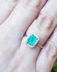 An emerald-cut emerald with a halo diamond ring on a person's hand.
