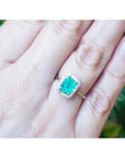 An emerald-cut emerald with a halo diamond ring on a person's hand.