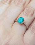 Emerald-cut Muzo Colombian emerald ring with a medium bluish-green gemstone set in a gold band on a hand.