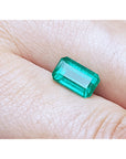 Emerald-cut natural loose colombian emerald, front position table and crown visibles between two fingers