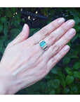 Emerald-cut men's emerald ring with side diamonds, bezel set in 18K white gold on a hand.